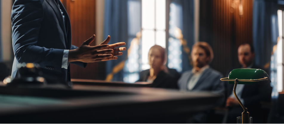 A courtroom with a blurred background of three people sitting in a row, facing one person standing with his hands open.